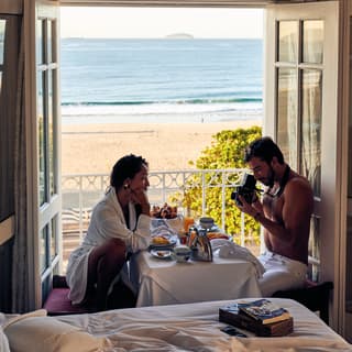 A couple sitting by the window in a suite taking picture of the breakfast