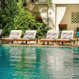 Sunbeds with palm print cushions lining a glittering outdoor pool