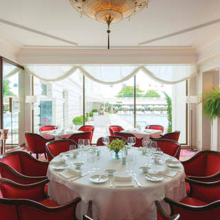 Red club chairs surround circular tables in an elegant dining room, with red floral carpet, white tablecloths pool views