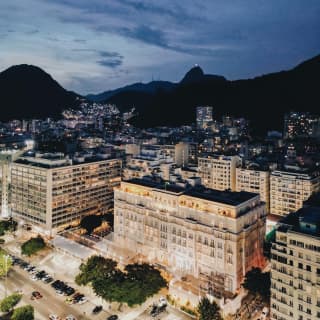 Copacabana Palace sparkles at night, with a backdrop of neighbouring buildings and dramatic black mountains, seen from above.