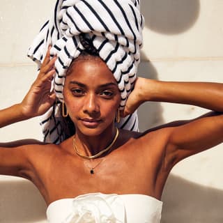 A woman facing the camera while holding her hair wrapped in a black and white striped towel