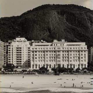 A vintage image of the hotel's facade and beach with the forested mountain behind shows almost no difference to today
