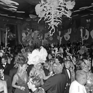Giant butterflies hang from the ceiling and walls. Party-goers in carnival costumes and black tie fill the ballroom and dance