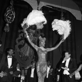 A samba dancer in carnival costume holds ostrich feathers aloft as she dancers to the rhythm of the live band behind her