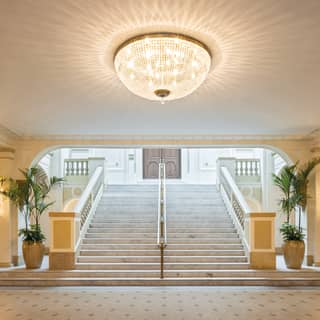 Spacious and light theatre foyer with a grand chandelier and marble steps 
