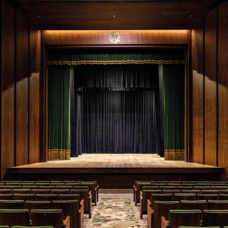 Rows of green theatre chairs facing a grand stage with emerald theatre curtains