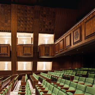 Spacious walnut wood-panelled theatre with rows of green chairs and balcony seating