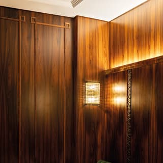 Glowing art-deco wall lamp with golden detailing reflecting light on walnut panelling