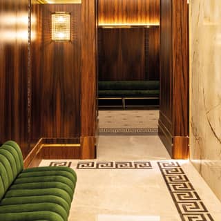 A polished wood panelled doorway leads through a marble wall to additional green velvet bench seating