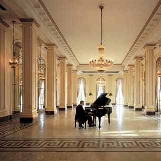 Pianist playing a piano in an empty grand ballroom with a mosaic floor
