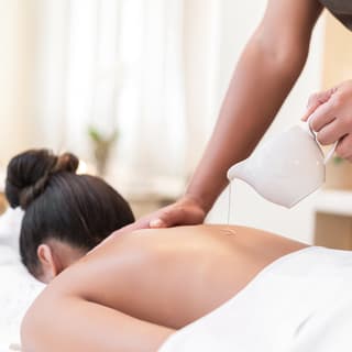 Lady lying on a massage table and having warm oil poured onto her back