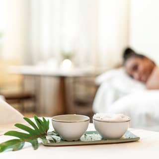 Two gold rimmed coffee cups rest on a small green ceramic tray, decorated with a palm leaf, in a fresh spa treatment room