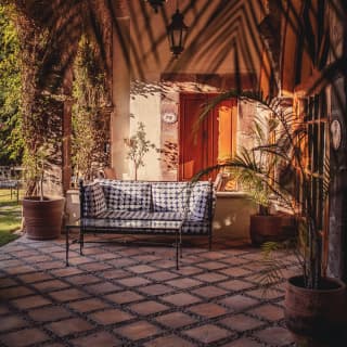 View beneath the beamed roof of Casa Palma's terracotta terrace, with sofa, walls and plants aglow in dappled evening sun.