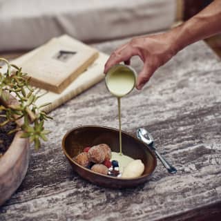 Close-up of custard being poured into an oval bowl of donut balls