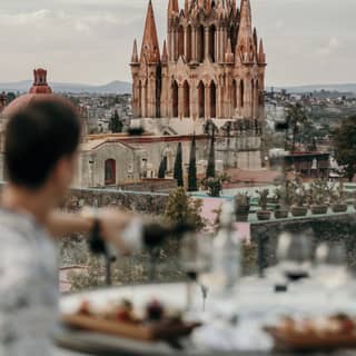 a man pouring wine at the terrace of the Casa de Sierra Nevada hotel's rooftop overlooking La Parroquia de San Miguel Arcángel church in the background