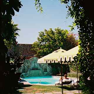 A guest relaxes on a chair by the sparkling pool in the hotel's walled garden, seen through an arch clad with climbers.