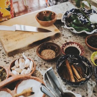 Pupils de-stalk green herbs at a marble-top workspace filled with small bowls containing garlic, salt, cinnamon and spices.