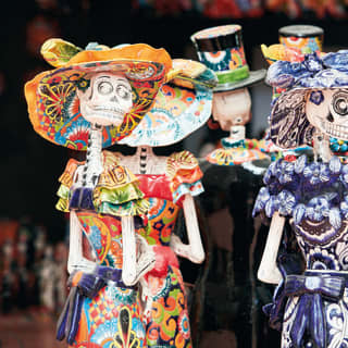 Rows of vibrantly-coloured ceramic 'day of the dead' figurines in patterned dresses and hats