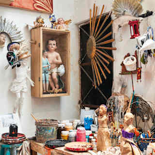Studio with an eclectic collection of papier-mache art pieces and a bench brimming with paint bottles