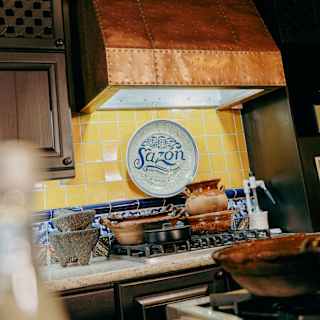 Angled view of the Sazón Cooking School hob piled with earthenware pots below a copper extractor.