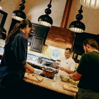 Angled image of two students preparing ingredients at a counter opposite Chef Ruben Yañez at Sazón Cooking School.