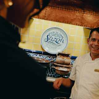 Chef Ruben Yañez smiles as he takes a class, in an angled shot that captures a Sazón Cooking School-branded wall plate.