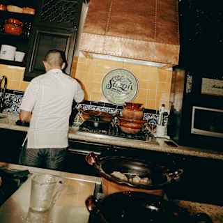 Chef Ruben Yañez, in a white top, works at a counter to the left of a cooking hob, seen from behind at Sazón Cooking School.