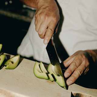 Angled close-up image of a chef as he slices fresh wedges of avocado on a thick chopping board.