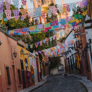 Angled image of the spires of Parroquia de San Miguel Arcángel rising behind a street fluttering with papel picado bunting.