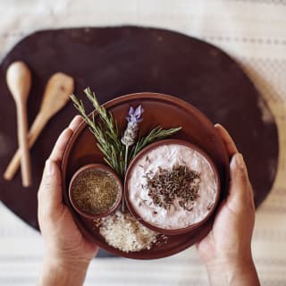 Two hands holding a bowl of spice and herb ingredients for a poultice