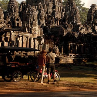 Two tourists standing on the grass in front of Angkor Thom temple to admire it