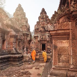 Zwei Mönche in orangefarbenen Roben inmitten eines verzierten Khmer-Tempelkomplexes