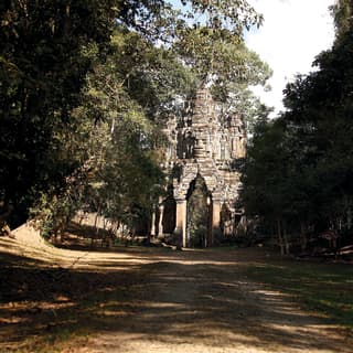 Vast stone temple gate carved with a god-like figure and lined with trees