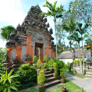 A Kori Agung ornate stone entrance gate with orange walls and a narrow doorway with a Balinese god carving above the lintel.