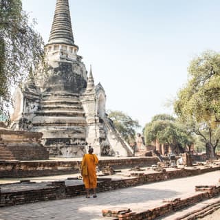 A monk in orange robes looks up at the conical peak of a stone monument in Ayutthaya's holy temple of Wat Phra Si Sanphet.