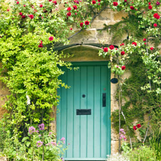 Idyllic sandstone cottage with a mint green wooden door surrounded by red flowers
