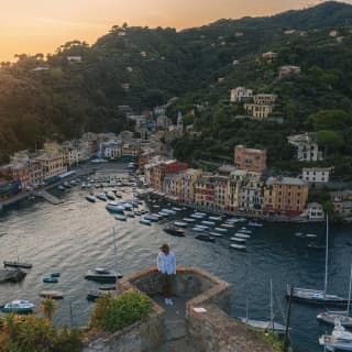 Man in a sunhat peering over the wall of a traditional fort towards Portofino piazzetta