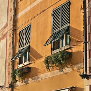 On the ochre-painted face of a Portofino townhouse, two sets of green shutters are propped open above trailing window boxes.