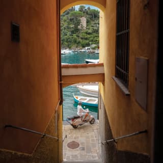Narrow view between two town houses of a vespa driver beside Portofino harbour