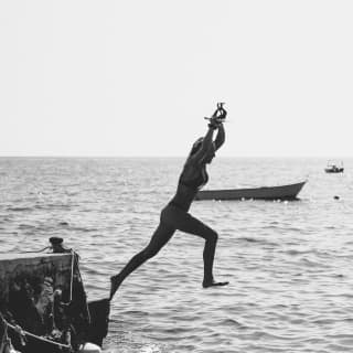 Black and white photograph of a lady in swimwear leaping from a pier into a harbour