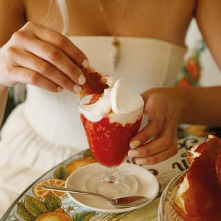 A blond woman dips a hunk of brioche into a glass of strawberry granita at a lemon-patterned table at Bam Bar in Taormina.