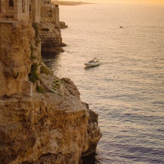 a boat sailing by the rocky coast line at sunset