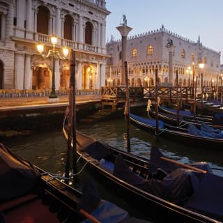 Gondolas moored along the Riva degli Schiavoni waterfront where the ornate, marble Doge's Palace is lit up in the lilac dusk.
