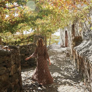 Lady in a summer dress walking along a cobbled path under the shade of trees
