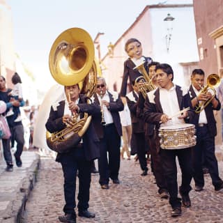 Banda mexicana desfilando por calles adoquinadas con tambores y un trombón