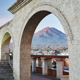 A row of stone arches inscribed with latin framing the mountain beyond at sunset