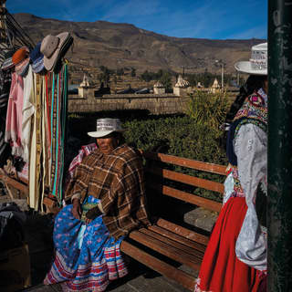 A local woman, dressed warmly, sits on a bench by her stall, selling hats and fabrics in Yanque, in Peru's Colca Canyon.