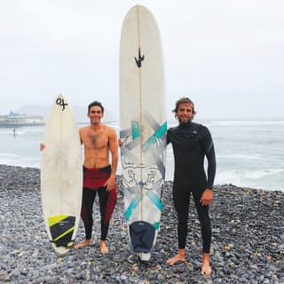 Two surfers standing on a stoney shore holding their surfboards upright