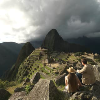 A couple sitting on a rock overlooking the Machu Picchu Inca citadel