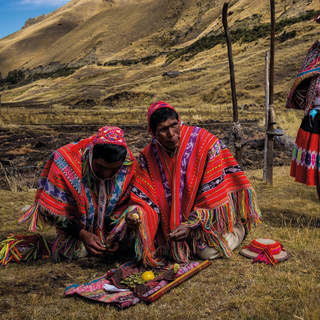 At a farm in the Sacred Valley, two men plant seed potatoes in tasselled shawls and two women stand by in traditional dress.